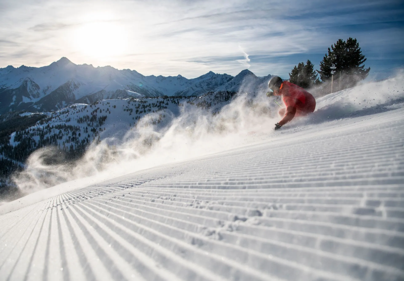 Skiër maakt een bocht door verse sneeuw op een geprepareerde piste